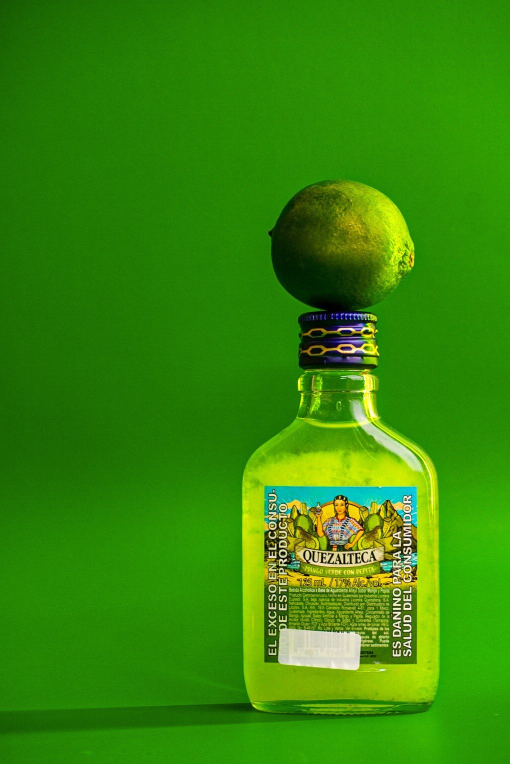 Botella verde con un limón encima sobre fondo verde